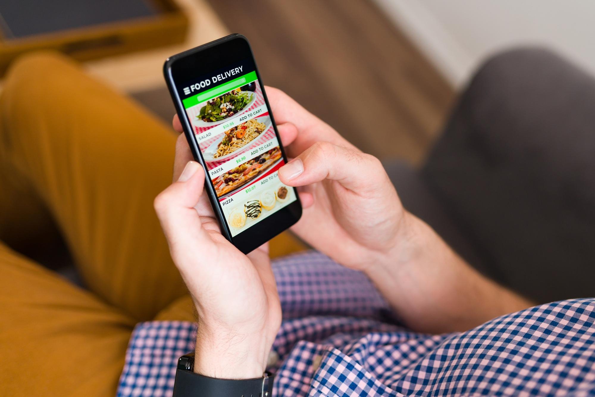 Homem mexe no celular em aplicativo de delivery em busca de um prato saudável
