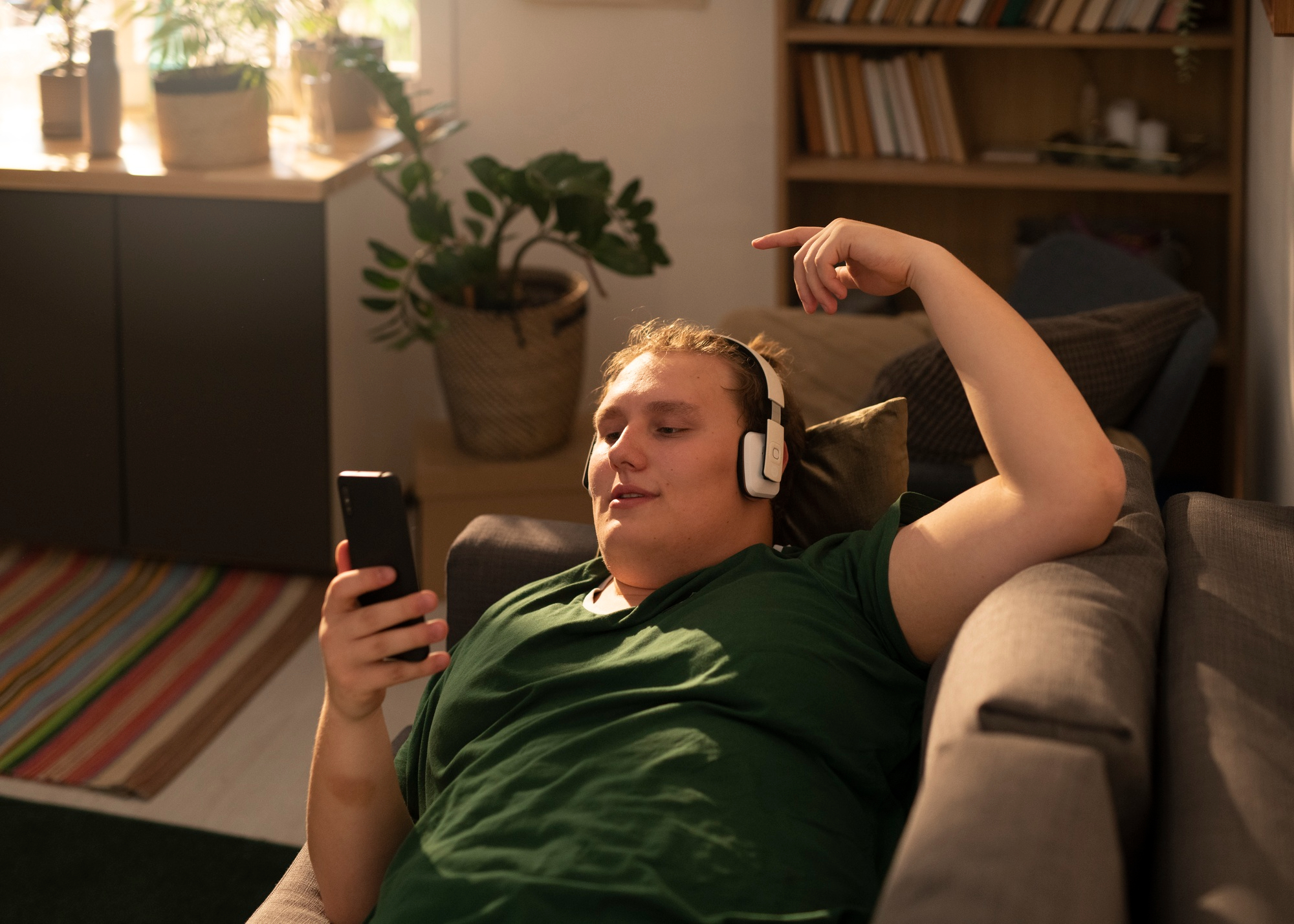 Pessoa sedentária deitada em um sofá, usando fones de ouvido e olhando para o celular, em um ambiente doméstico.