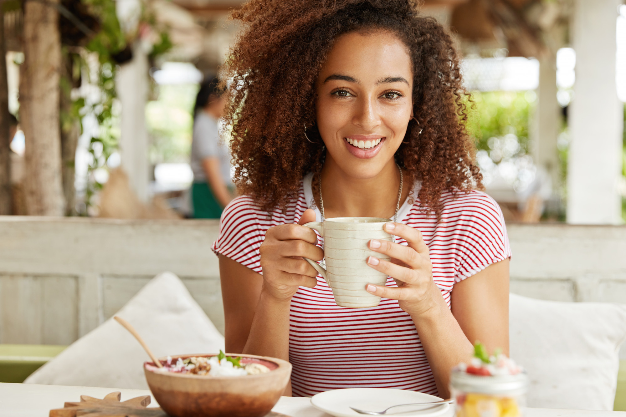 Mulher tomando café e comendo bolacha durante um café da manhã sem lactose em ambiente aconchegante.