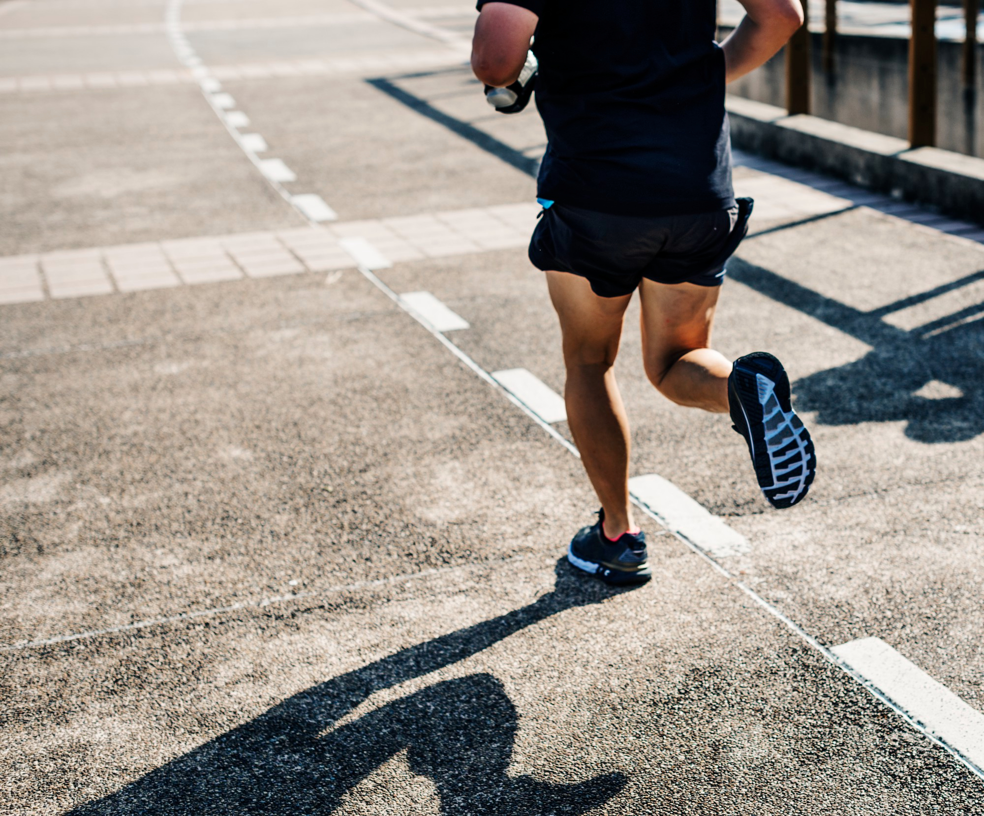 Pessoa correndo ao ar livre em pista asfaltada, usando roupas esportivas e tênis de corrida, representando prática de exercício físico.