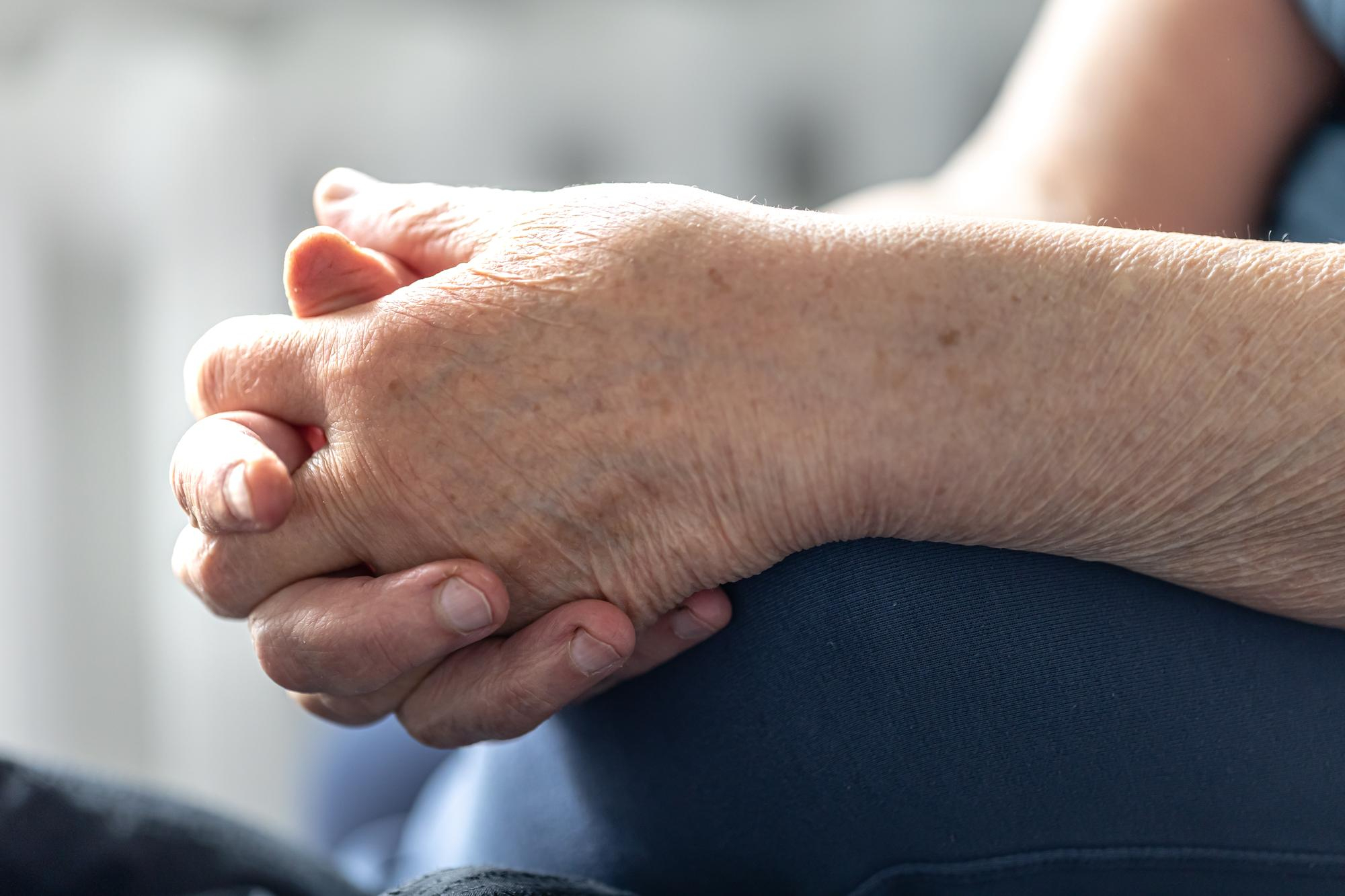 Imagem de pessoa idosa com as mãos cruzadas sobre o joelho em sinal de gota, doença causada pelo excesso de ácido úrico