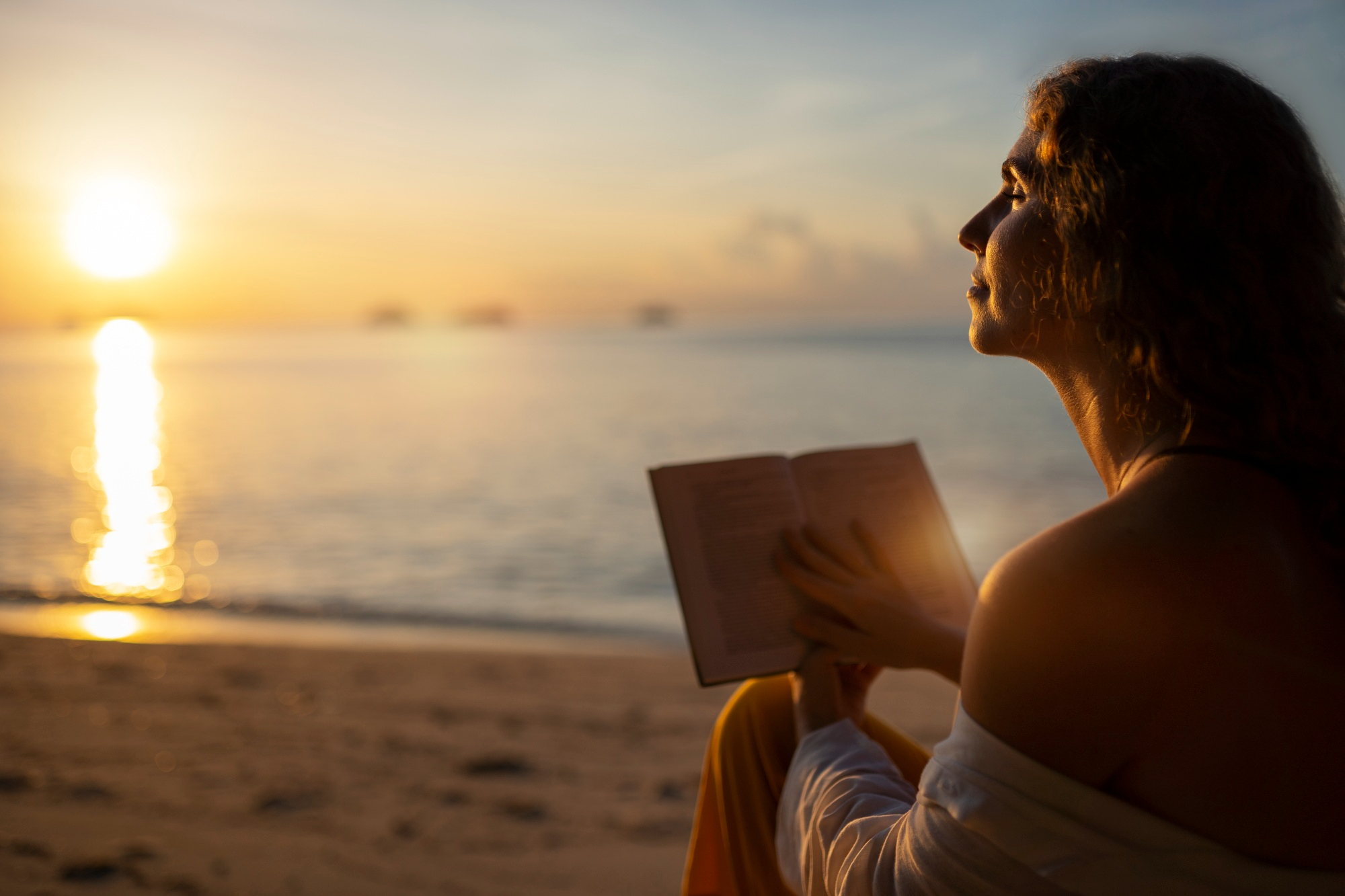 Mulher descansa a mente ao ler um livro na praia durantes as férias apreciando o pôr do sol