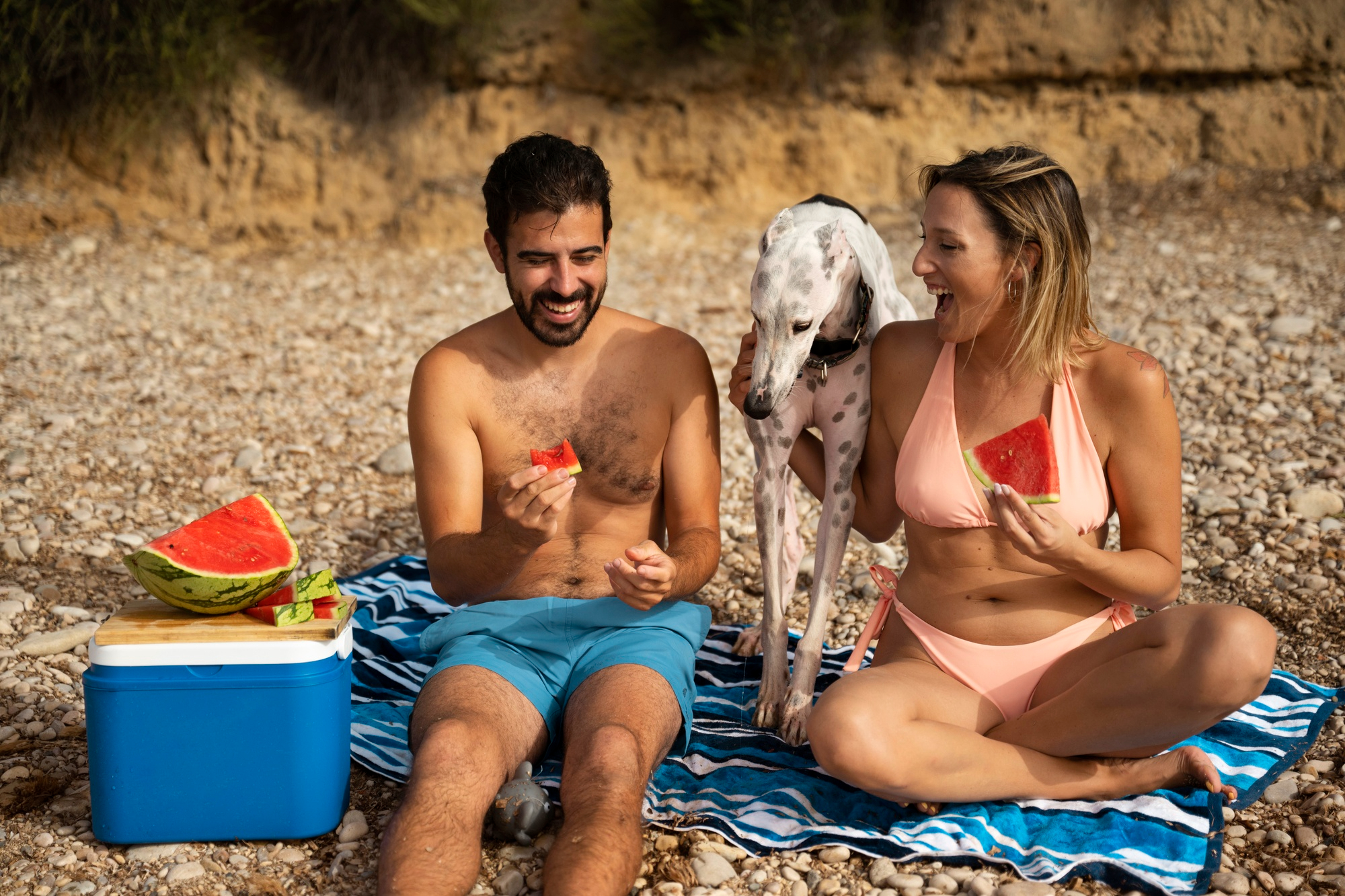 Casal jovem, homem e mulher comem melancia na praia durante o verão e tomam cuidado com intoxicação alimentar