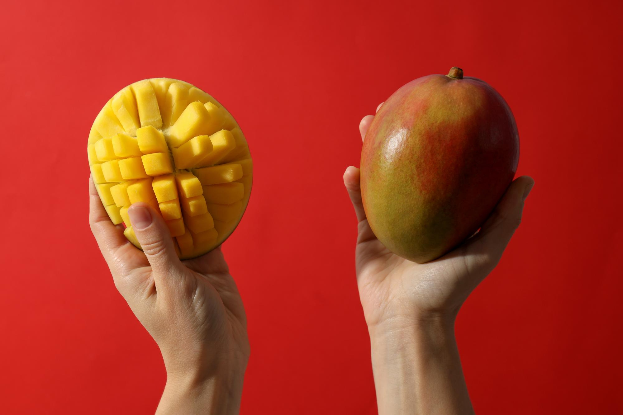 Mãos seguram duas mangas, uma cortada em cubos e outra inteira
