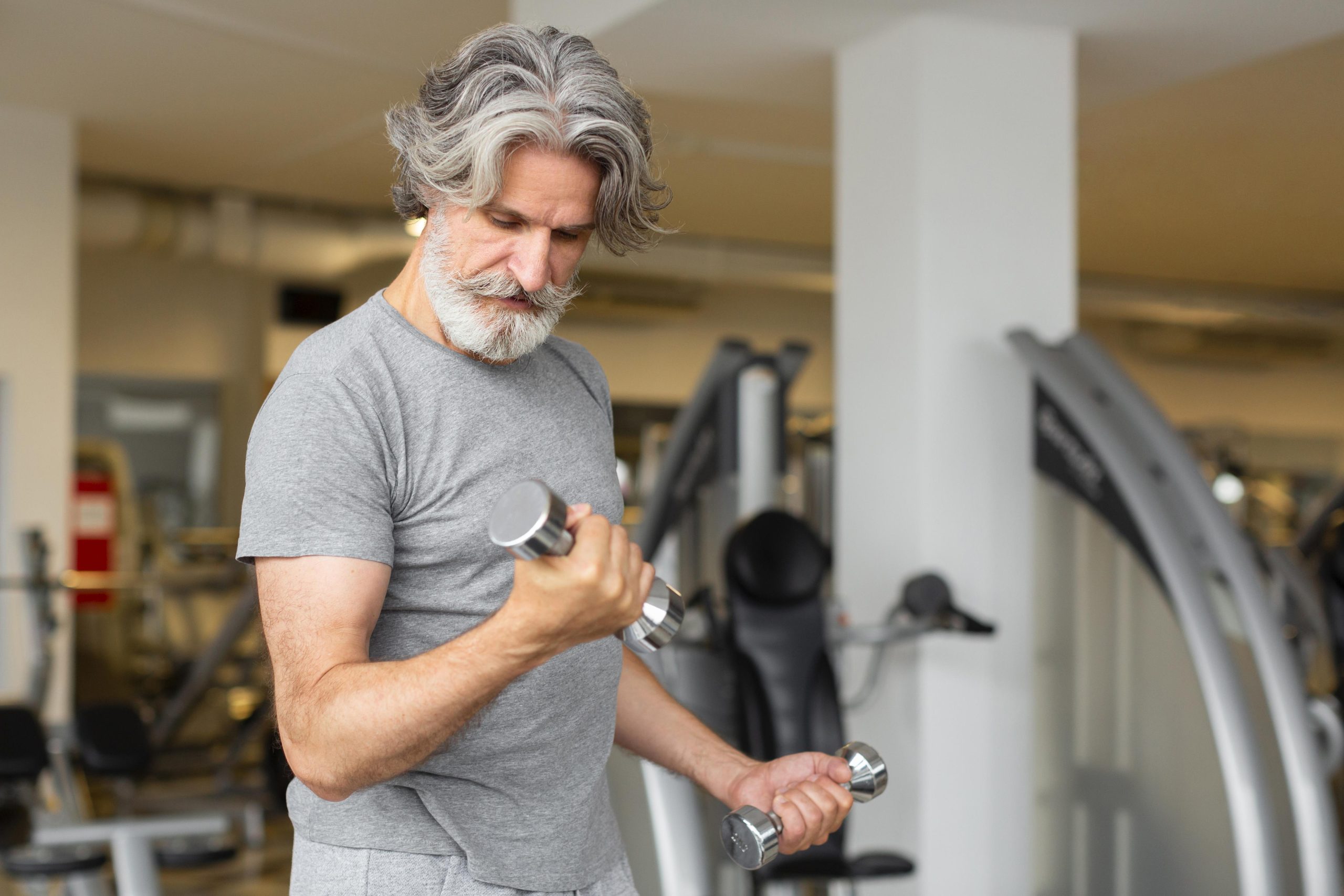 Homem treinando com halteres em academia durante exercício de musculação.