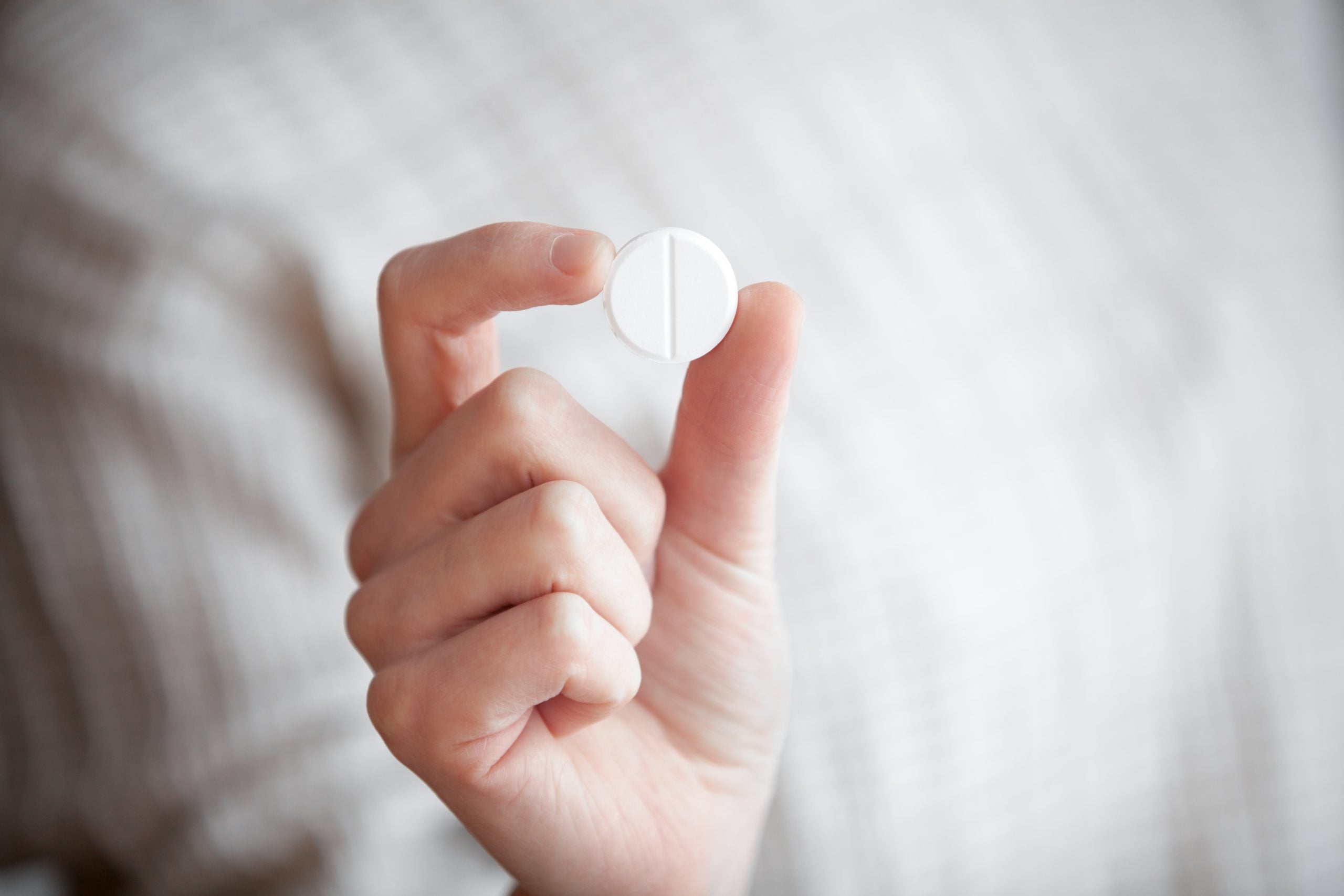 Mulher segurando uma pílula do dia seguinte entre os dedos, ilustrando o método de contracepção de emergência utilizado para reduzir o risco de gravidez após uma relação sexual desprotegida.