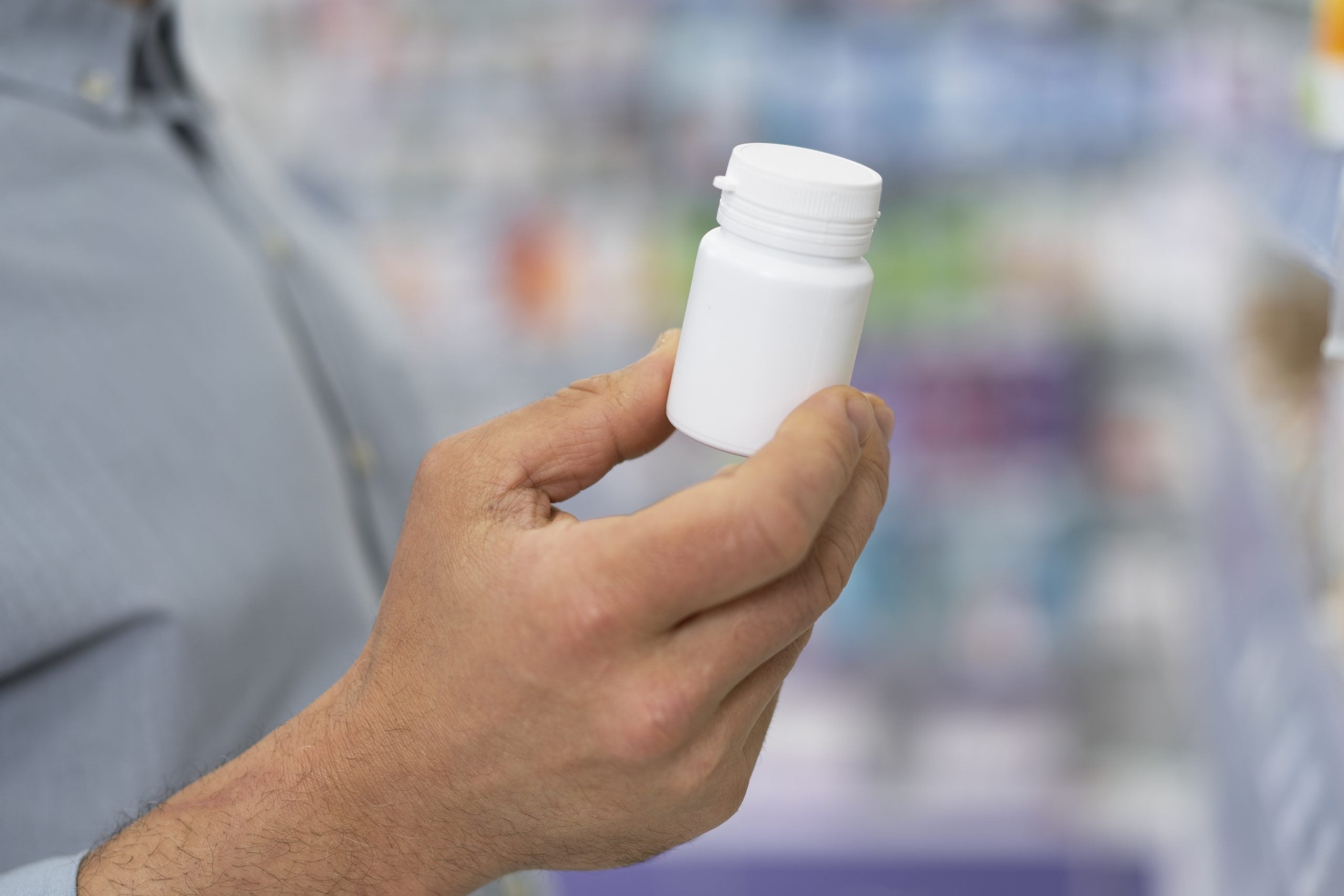 Pessoa segurando um frasco de medicamento em uma farmácia, ilustrando a importância de verificar a procedência e a autorização dos remédios.