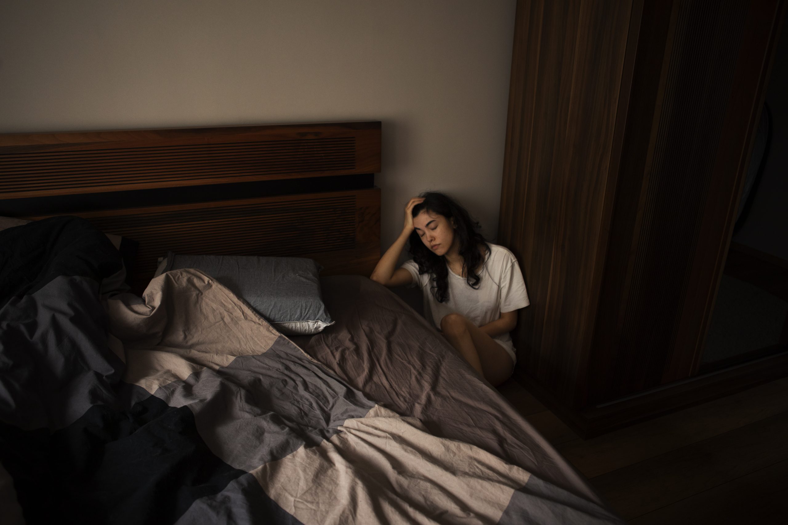 Mulher sentada ao lado da cama com expressão de sofrimento emocional, ilustrando um episódio de mania do transtorno bipolar e a necessidade de avaliação psiquiátrica para diagnóstico e tratamento adequados.