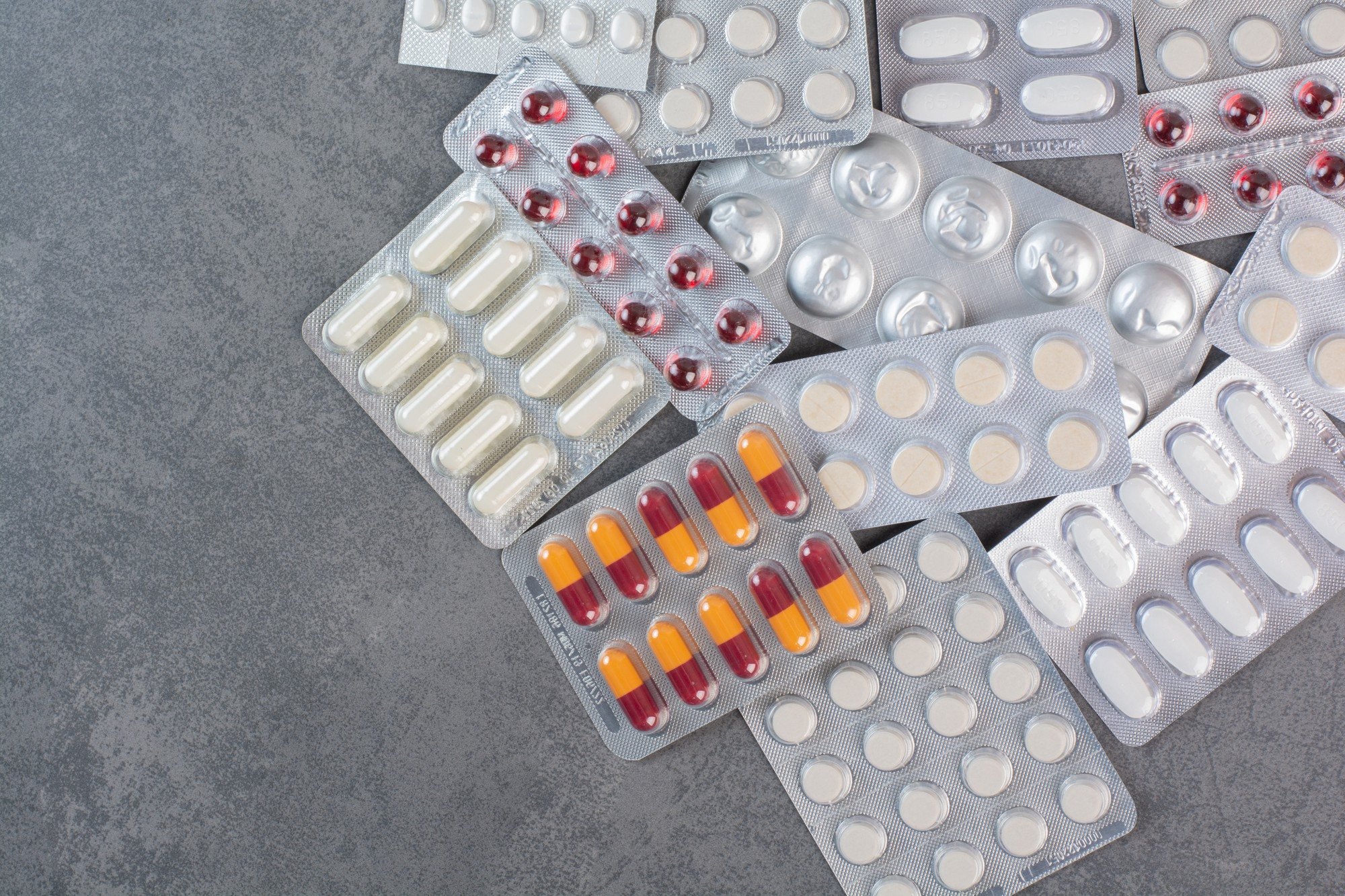 Diversas cartelas de comprimidos de anti-inflamatório dispostas em uma mesa cinza.