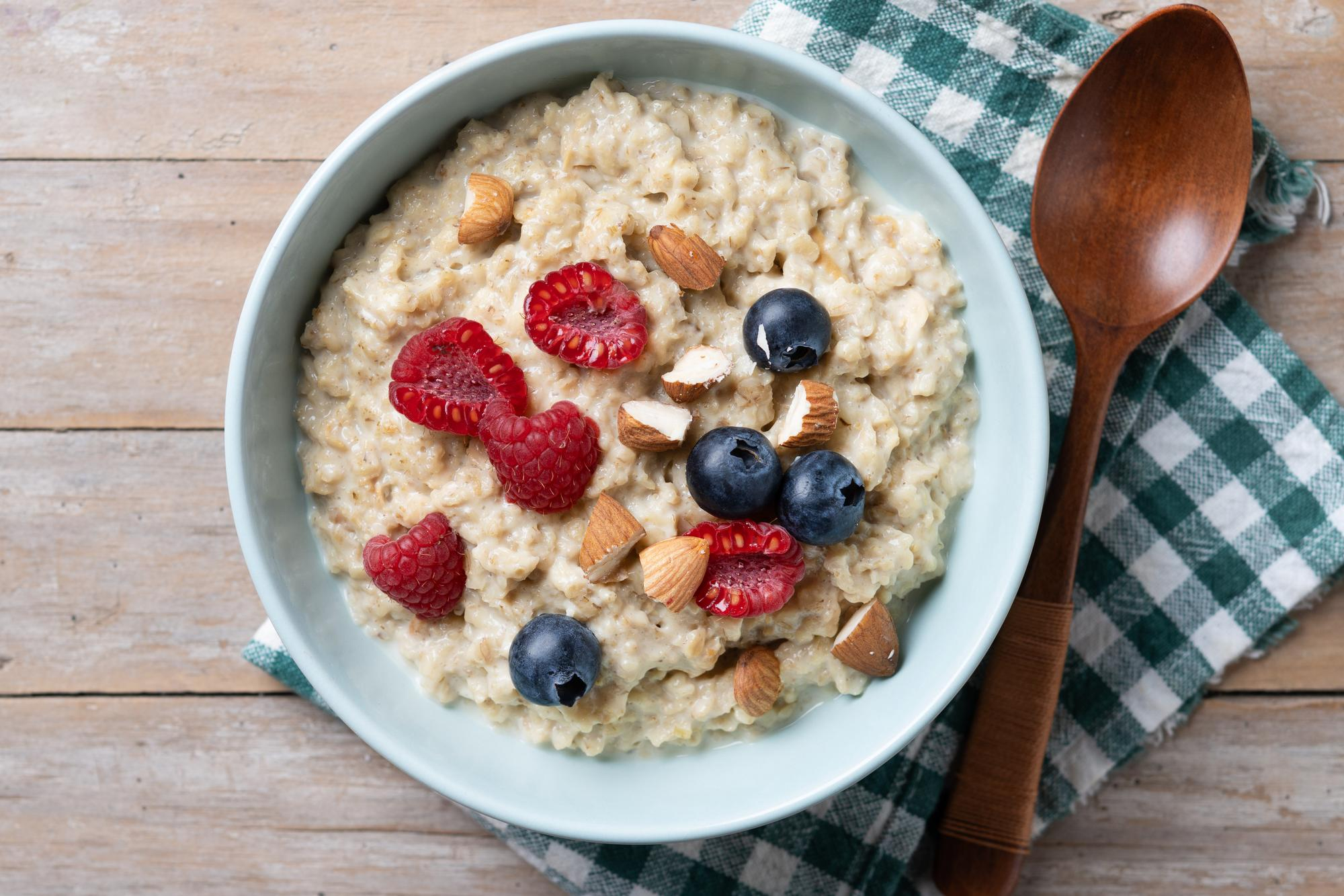 Tigela de mingau de aveia com frutas vermelhas e oleaginosas sobre uma mesa de café da manhã.