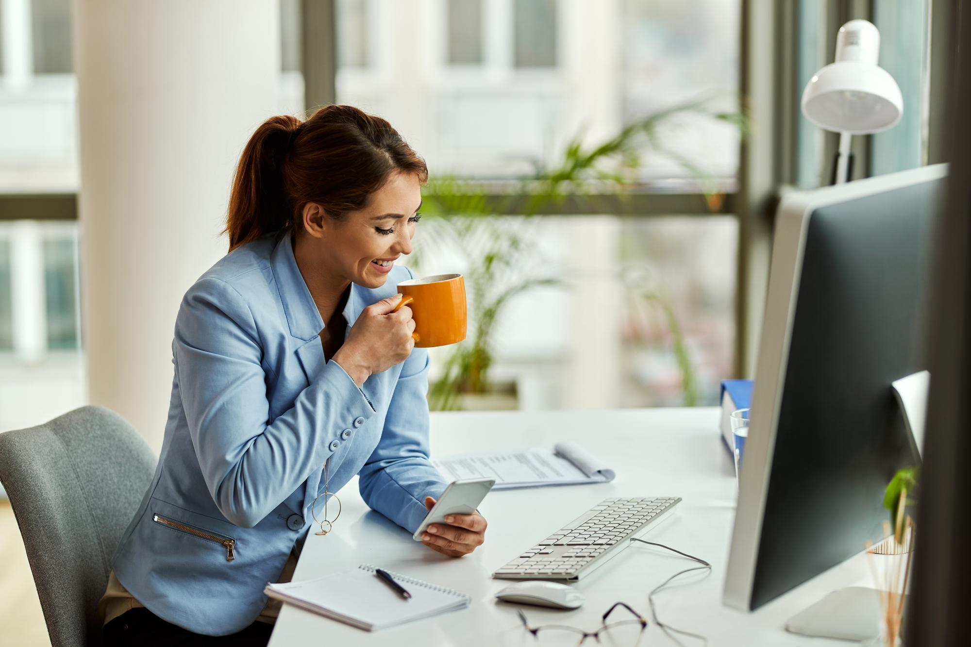 Mulher jovem trabalhando no computador enquanto toma uma bebida quente sem café.