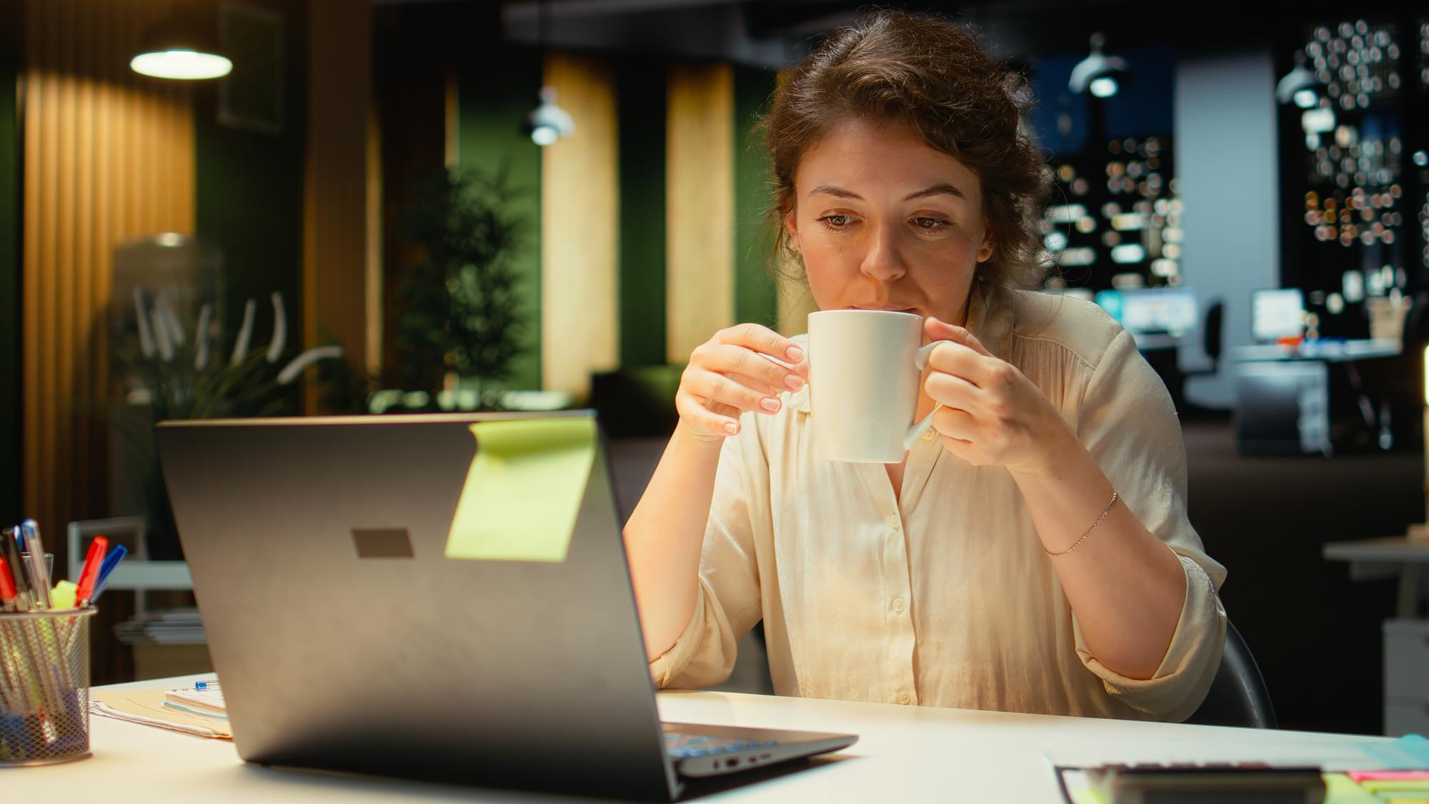 Mulher tomando uma xícara de café no fim da tarde enquanto trabalha.