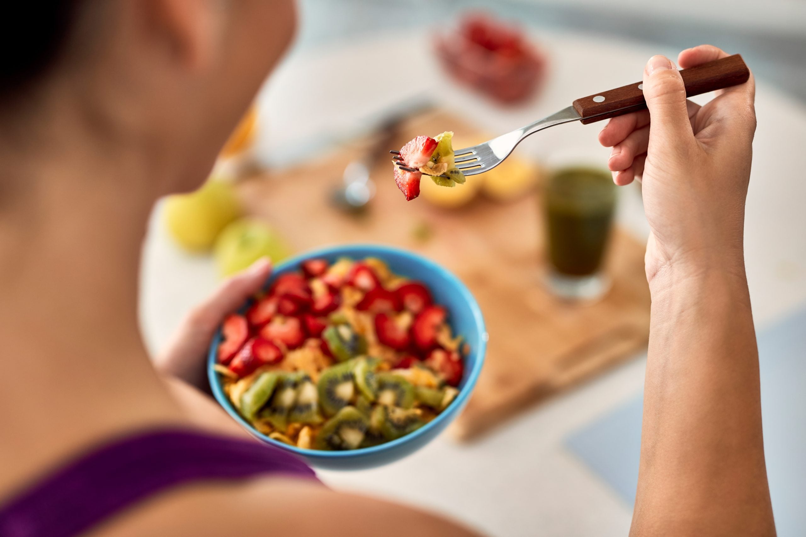 Mulher comendo uma salada de frutas com morango e kiwi, ilustrando as diferenças entre alimentos in natura, processados e ultraprocessados.