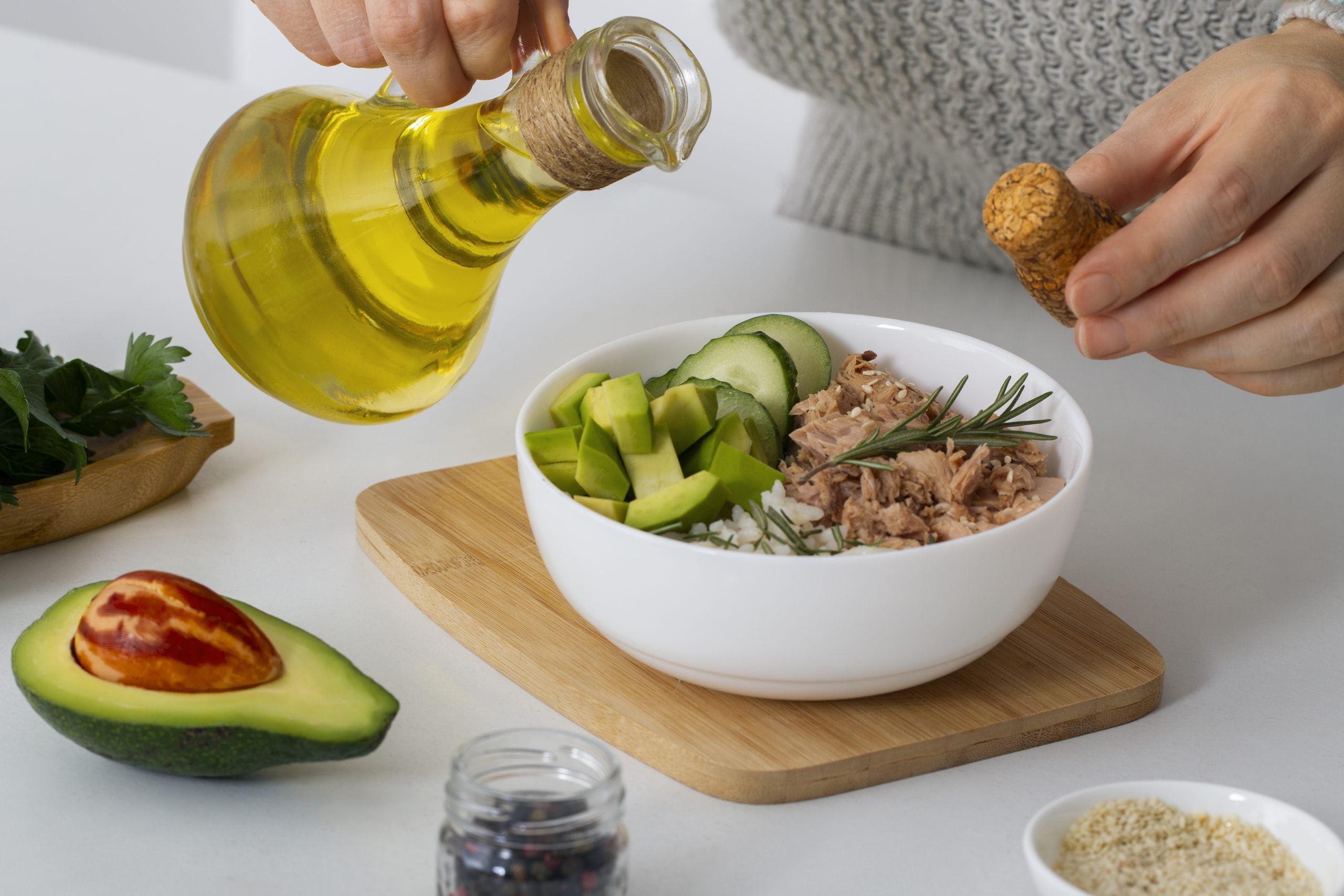 Pessoa preparando uma refeição com atum, abacate, pepino e azeite de oliva, alimentos ricos em proteínas e gorduras e com baixo teor de carboidratos, comuns na dieta cetogênica.