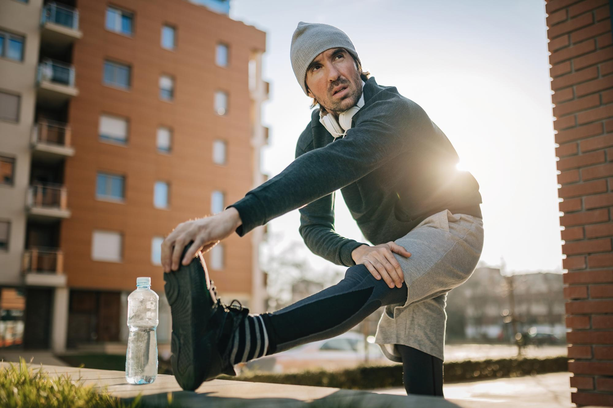 Pessoa alongando durante uma manhã fria de inverno, usando roupas apropriadas para exercício físico no frio.