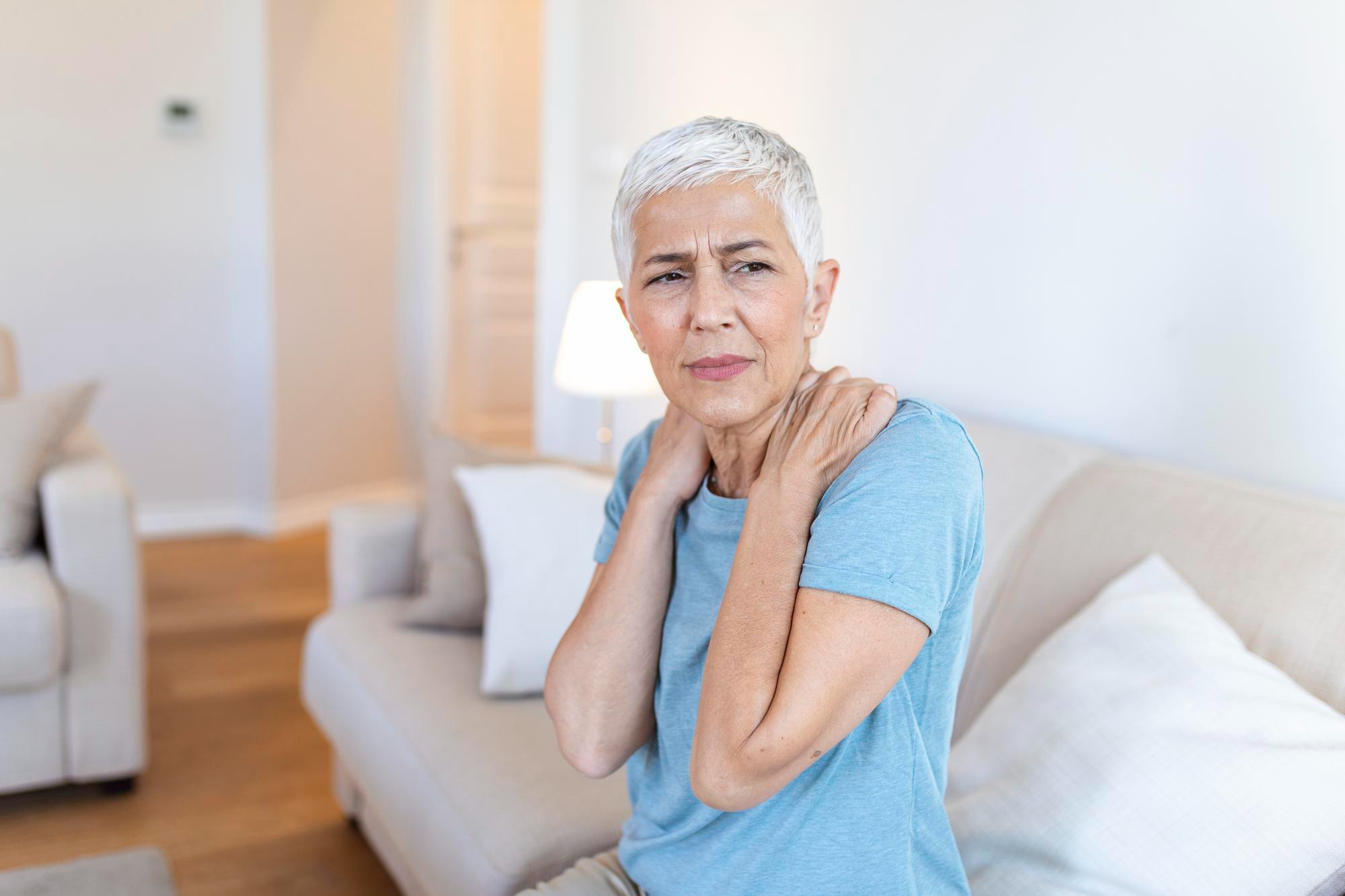 Mulher com dor muscular difusa, compatível com fibromialgia, coloca as mãos sobre os ombros.