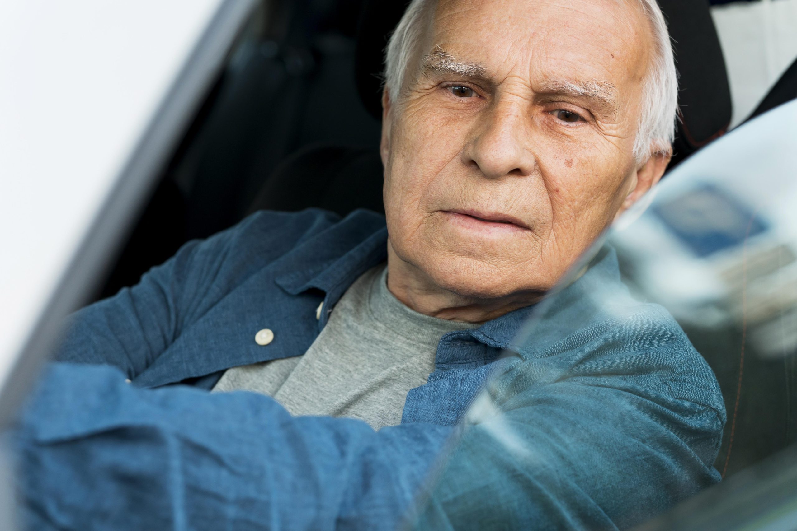 Homem idoso sentado no banco do motorista de um carro, olhando para a frente com expressão séria. A imagem ilustra a direção na terceira idade e a importância de avaliar a capacidade de dirigir com segurança ao longo do envelhecimento.