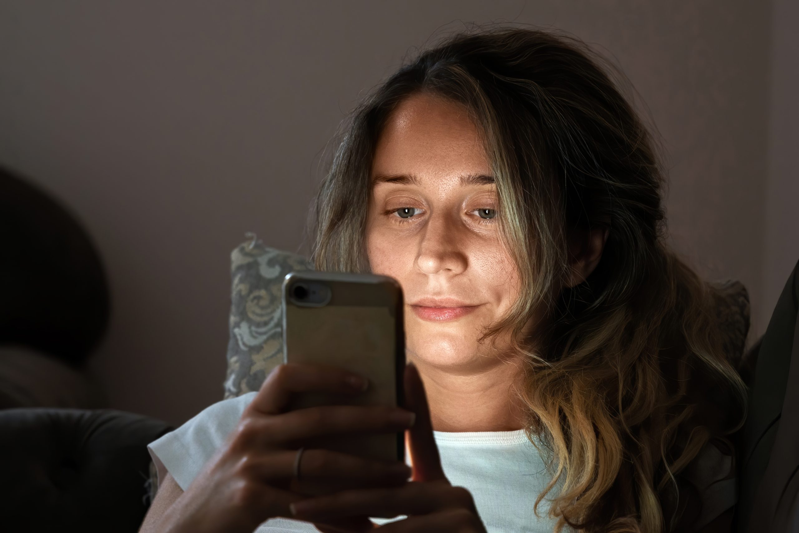 Mulher usa o celular na cama durante a noite, com o rosto iluminado pela tela; o uso excessivo de celulares e redes sociais pode afetar o sono, o descanso e a saúde mental na era digital.