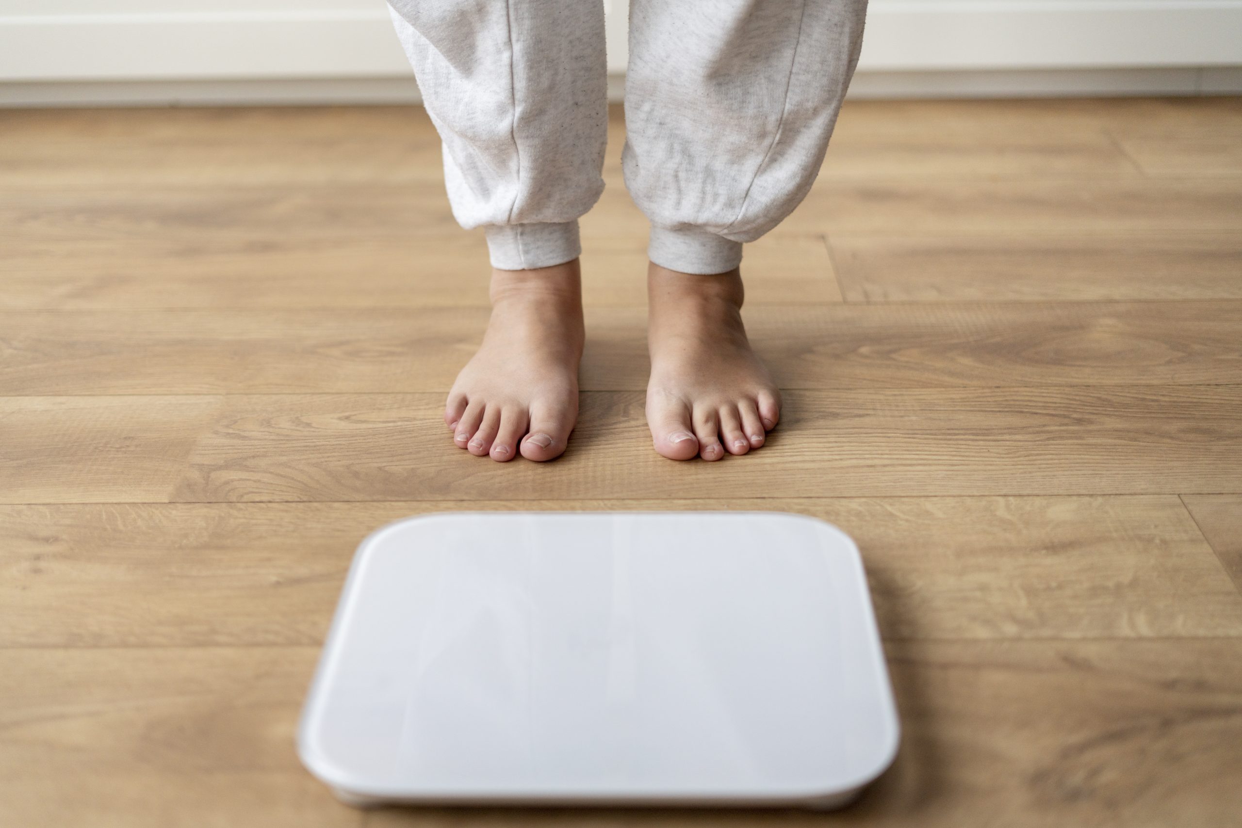 Pessoa em pé atrás de uma balança para acompanhar o peso corporal, uma das medidas usadas no cálculo do índice de massa corporal (IMC), que relaciona o peso com a altura, mas não diferencia a gordura da massa muscular.