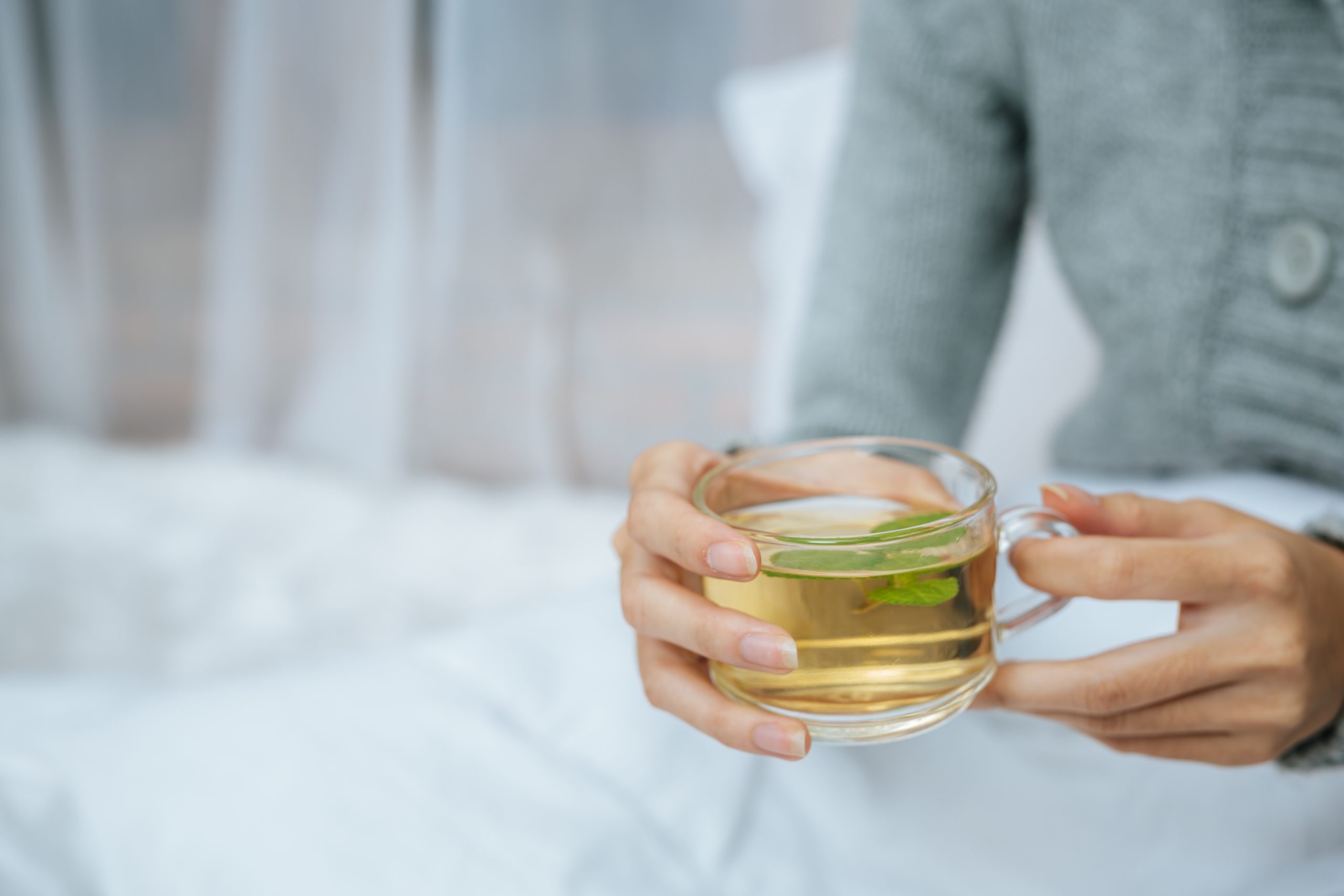 Pessoa segura uma xícara de chá verde, bebida termogênica com cafeína que pode acelerar os batimentos cardíacos em pessoas sensíveis.