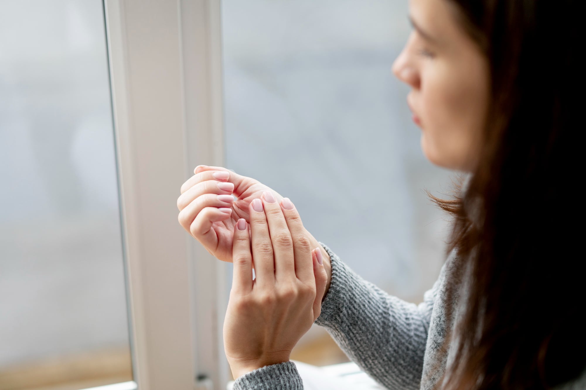 Mulher jovem observa unhas das mãos para avaliar se há alguma mudança nas unhas que possa indicar alguma doença.