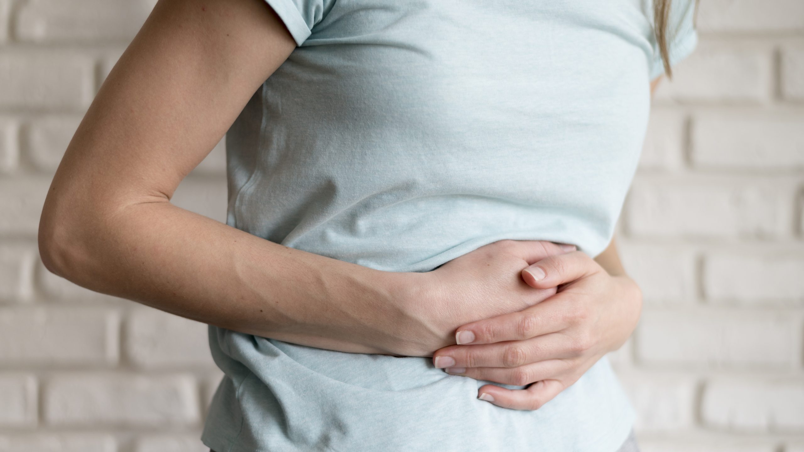 Mulher segura a barriga com as duas mãos enquanto sente desconforto abdominal, possível sintoma de intestino preso.