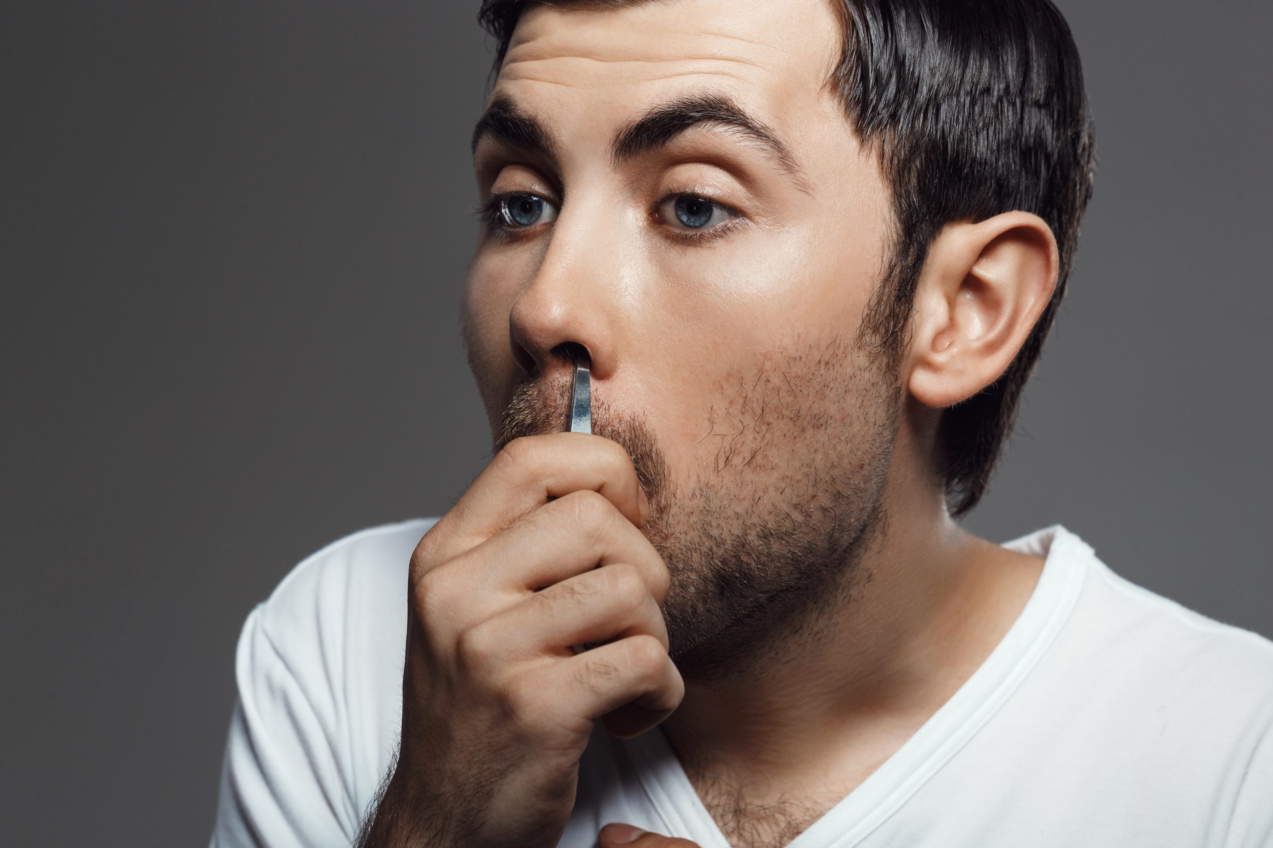 Homem usando uma pinça para retirar um pelo do nariz, hábito que pode causar pequenas lesões, irritações e infecções na região.